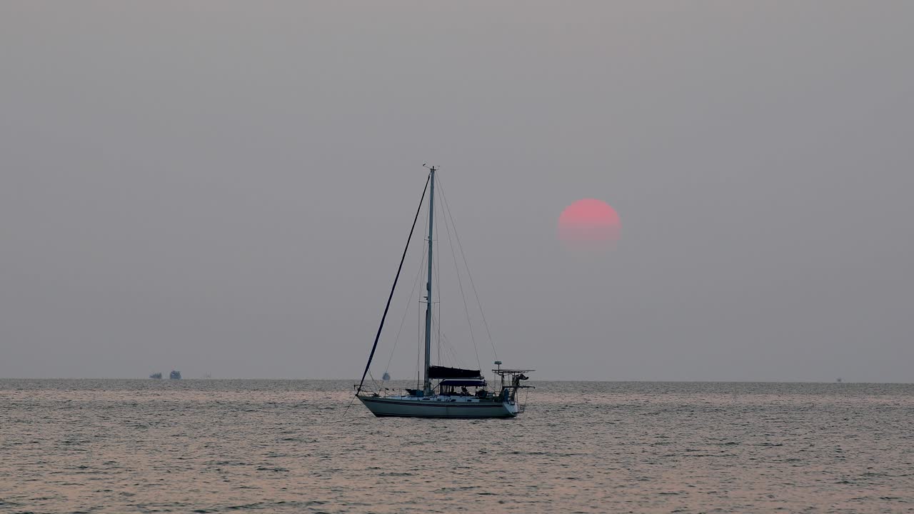 Beautiful Sunset with a Large Sun Going Down Behind a Yacht on the Horizon in Bangsaray near Pattaya, Thailand. Stationary Zoomed Shot in 4K