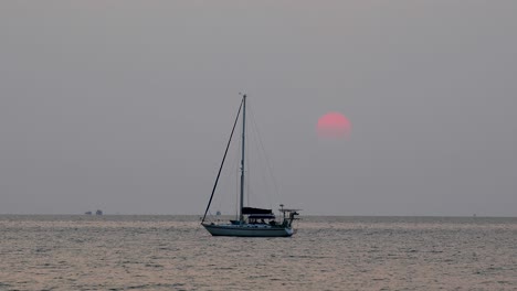 beautiful sunset with a large sun going down behind a yacht on the horizon in bangsaray near pattaya, thailand. stationary zoomed shot in 4k