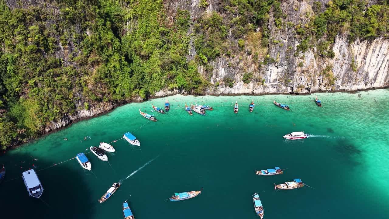 Riprese aeree con drone catturano barche longtail nelle acque turchesi della laguna di Pi Leh, circondate da imponenti scogliere calcaree di Krabi, Thailandia, sotto cieli sereni e soleggiati.