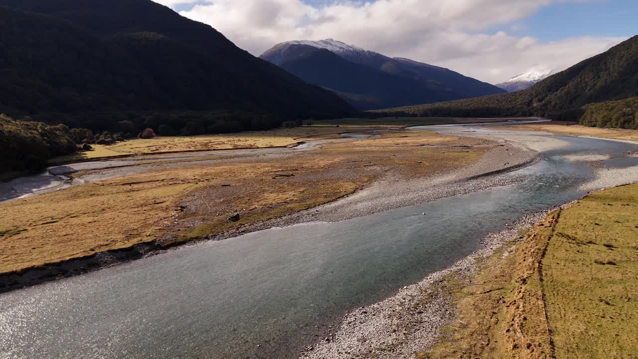 Drone flying low in semi dried river valley surrounded by dense majestic green mountains under cloudy sky