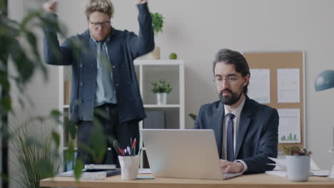 businessman working on laptop while colleague celebrates