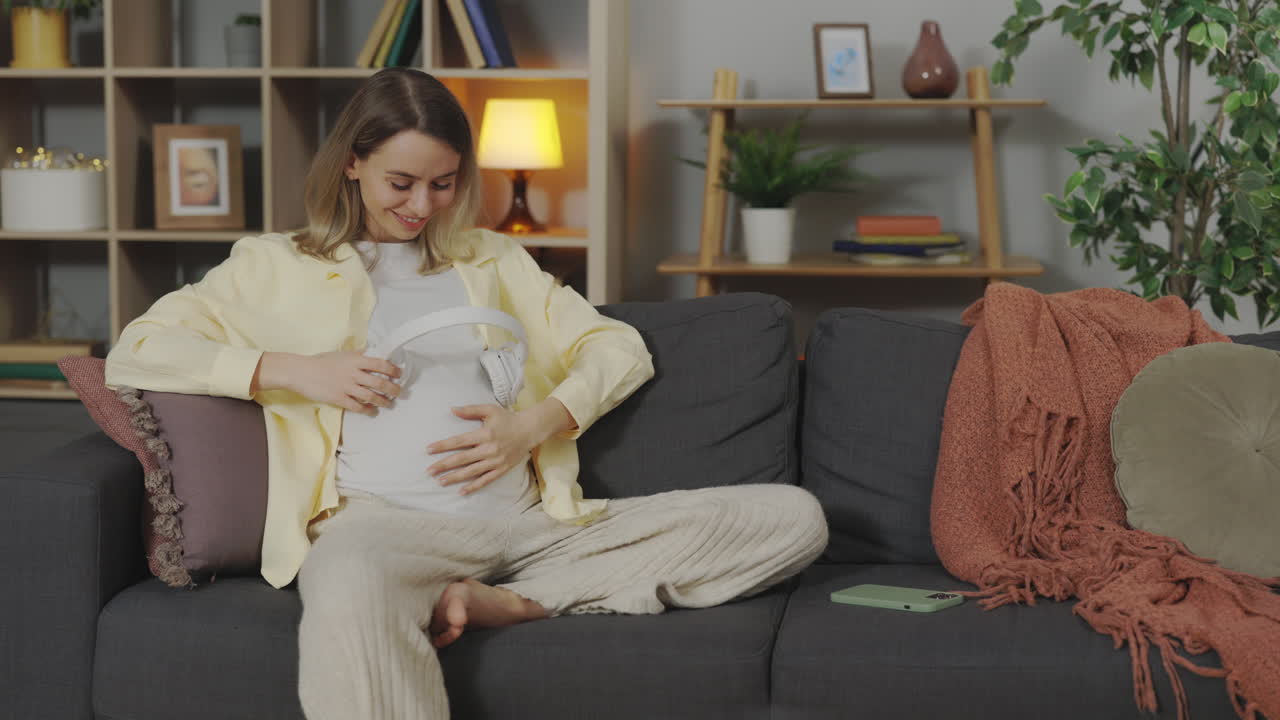 Pregnant woman listening to music on headphones at home