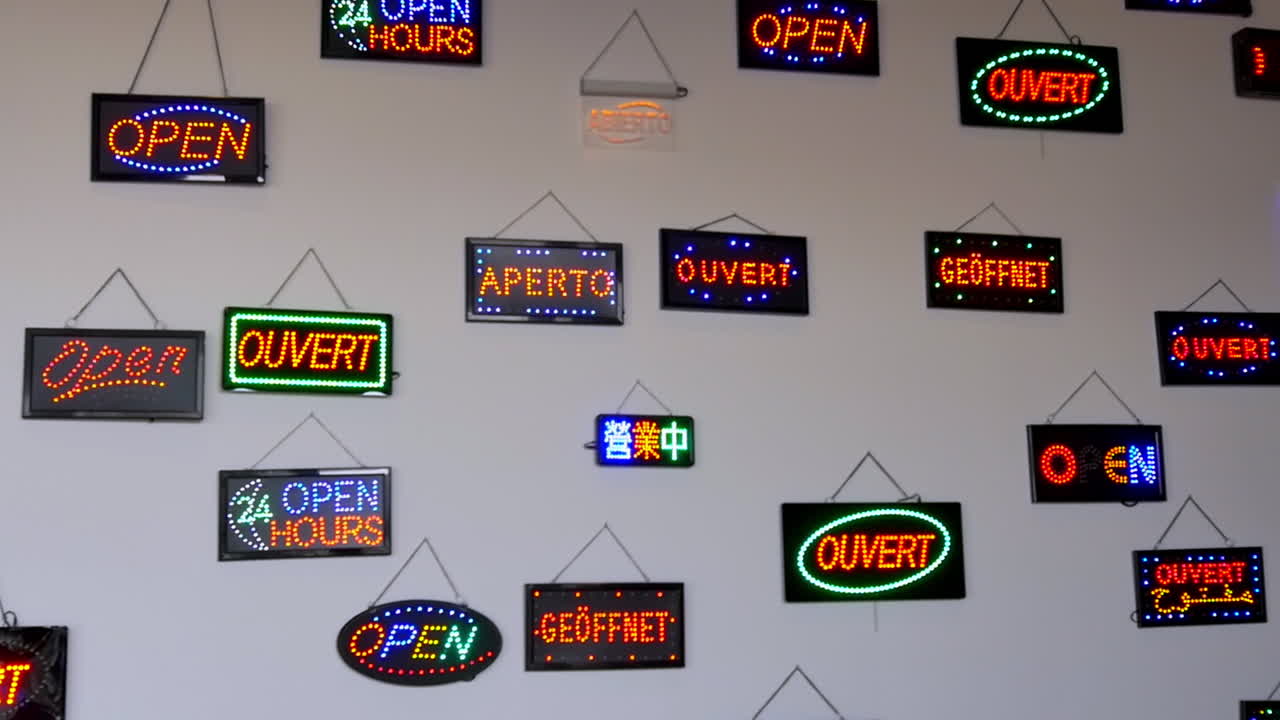 Colorful neon "open" signs in multiple languages hanging on a white wall, creating a vibrant and multicultural visual mosaic