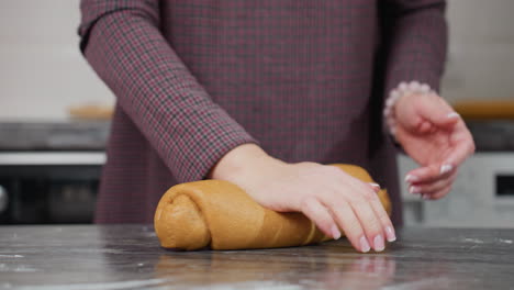 partial view of baker with bracelet on left hand kneading fresh dough on kitchen counter, modern kitchen setting, preparing homemade bread, rolling pin, white cabinets