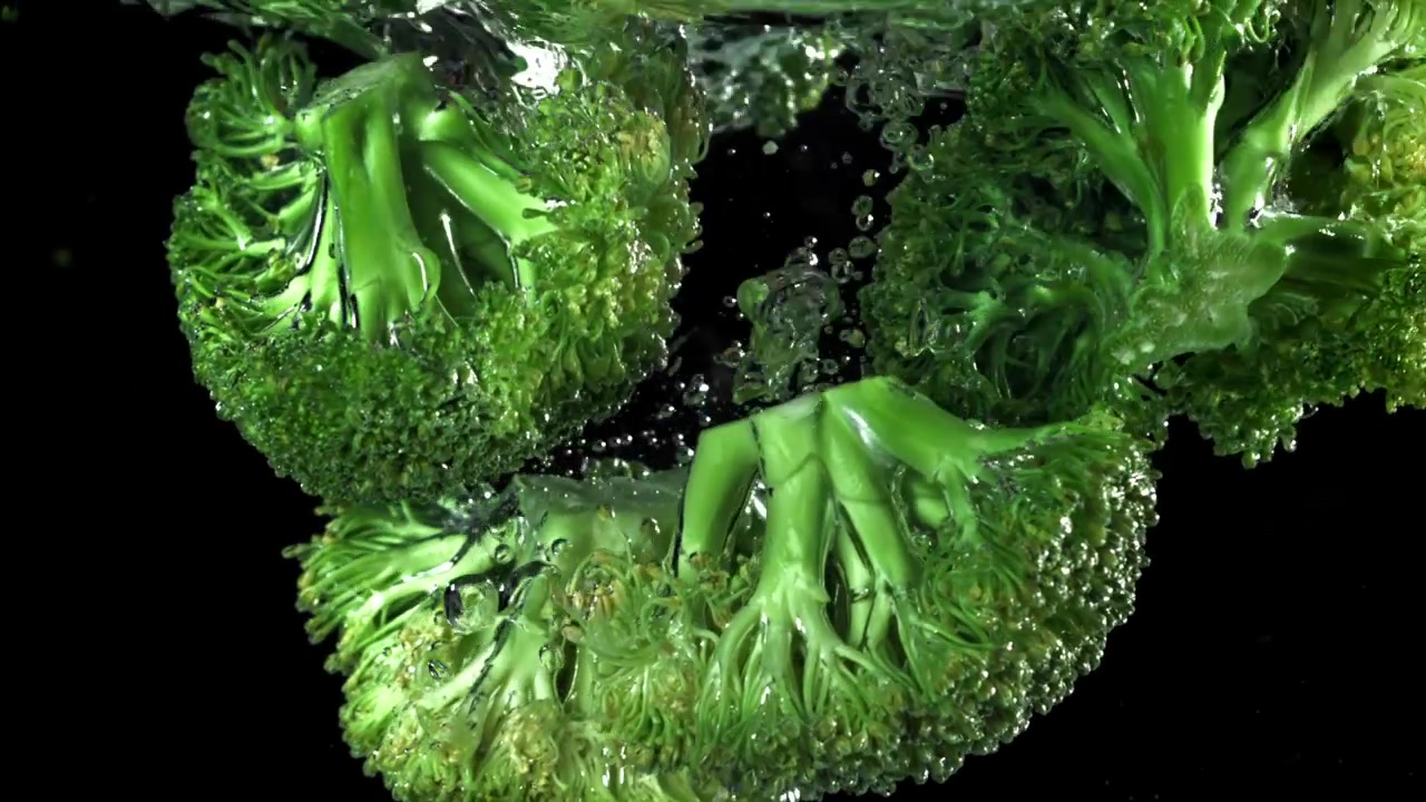 Cimette di broccoli freschi e verdi che cadono nell'acqua al rallentatore