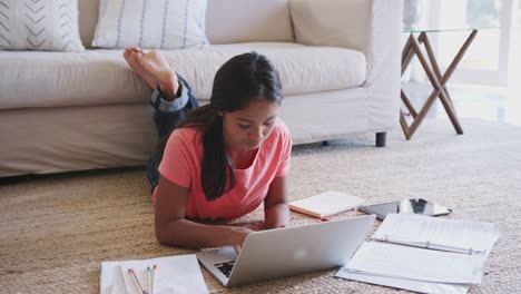 Teenage-girl-lying-on-the-floor-doing-homework-using-a-laptop-computer,-full-length,-elevated-view