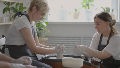 a female potter's wheel sculpting teacher explains how to work and teaches an elderly woman to work with clay and make mugs and jugs. master class for pensioners. pottery courses