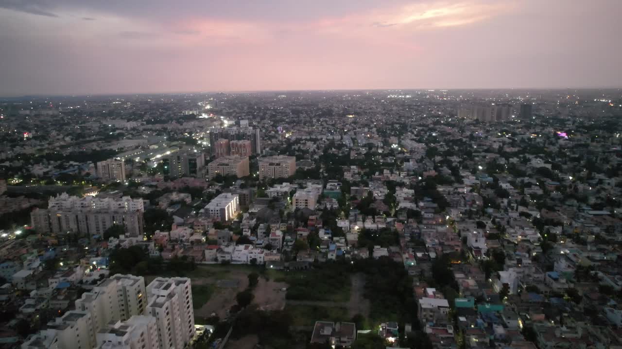una vista aérea nocturna de la ciudad de chennai revela un barrio lleno de gente, estructuras de gran altura, patio de recreo y carretera principal