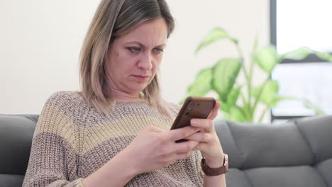 Woman looking at smartphone with a concerned or disgusted expression on a couch
