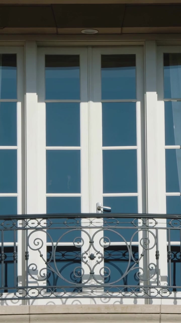 Vertical video: Showing white French doors facing road catching sunlight and revealing iron railing