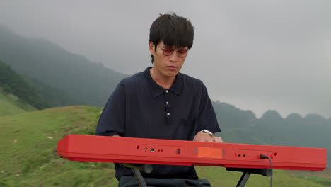 young vintage asian man with sunglasses playing piano on edge of the world