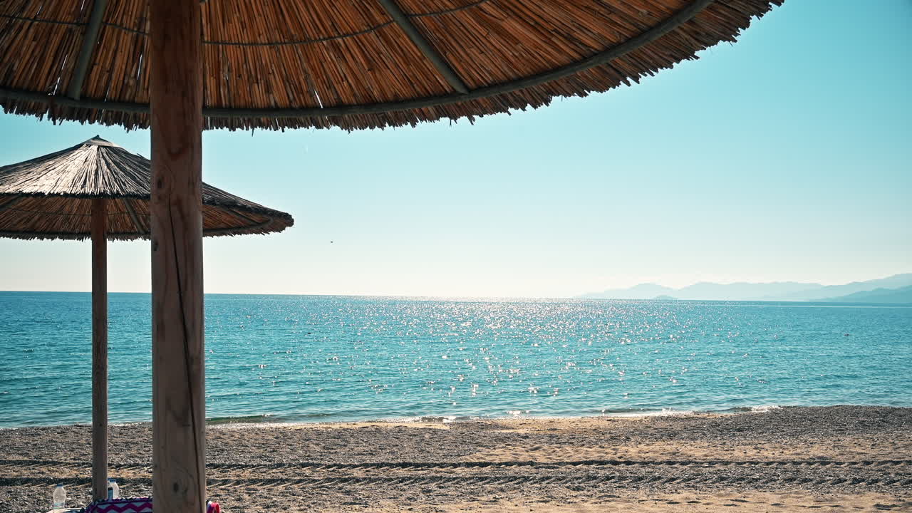 Spiaggia sulla costa dell'Egeo in Grecia. Ombrelloni, sabbia, mare blu, terra in lontananza