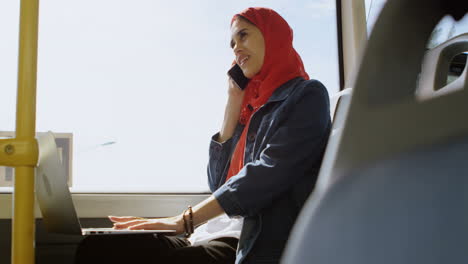 woman in hijab talking on mobile phone while using laptop 4k