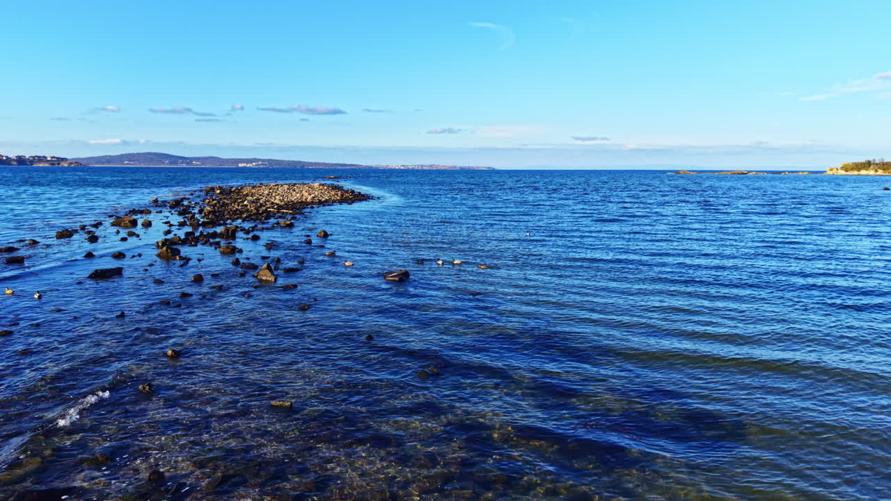 Malerische Aussicht auf ruhiges Wasser, das bei Sonnenuntergang unter einem klaren blauen Himmel auf eine felsige Küstenlinie trifft