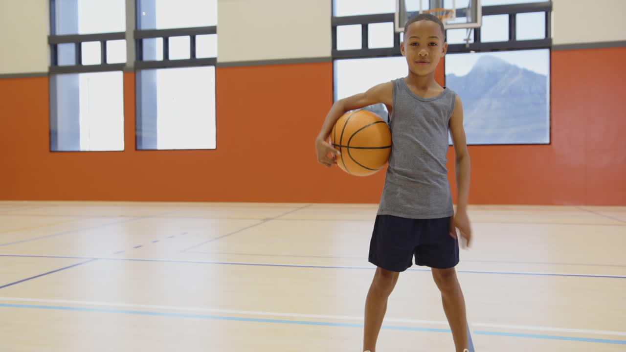 In school gym, boy holding basketball and smiling, ready to play