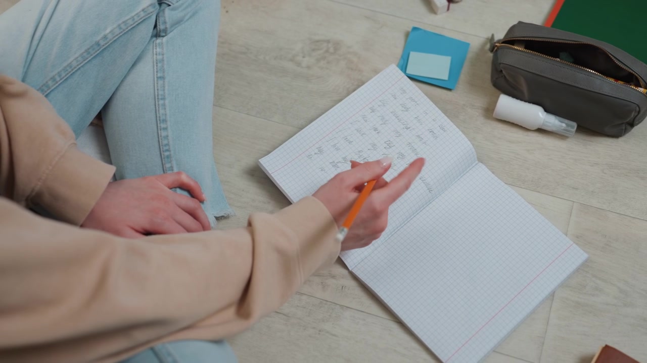 White woman arranging study notes on floor, pencil marking workbook, checklist and memo pad beside, preparing lesson for online coaching session, upbeat organized mood with natural sunlight