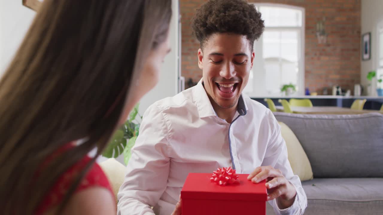 Happy biracial couple celebrating valentine's day giving presents at home