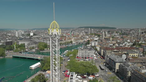 Un-Dron-Aéreo-Disparó-Un-Lento-Sobrevuelo-En-órbita-Alrededor-De-La-Torre-De-Caída-Libre-Del-Parque-De-Atracciones-Con-La-Ciudad-Y-El-Lago-De-Zúrich,-Suiza-En-El-Fondo-Durante-El-Zürichfest