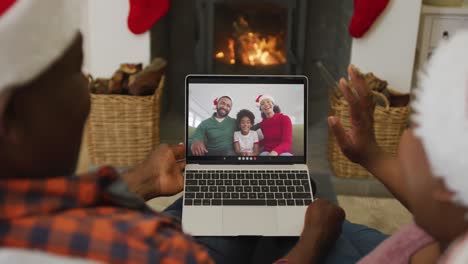 Afroamerikanisches-Paar-Mit-Weihnachtsmützen-Nutzt-Laptop-Für-Weihnachtsvideoanruf-Mit-Der-Familie-Auf-Dem-Bildschirm