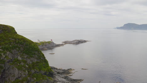 rocky cliff at the coast with a distant view of skongenes lighthouse in maaloy, norway