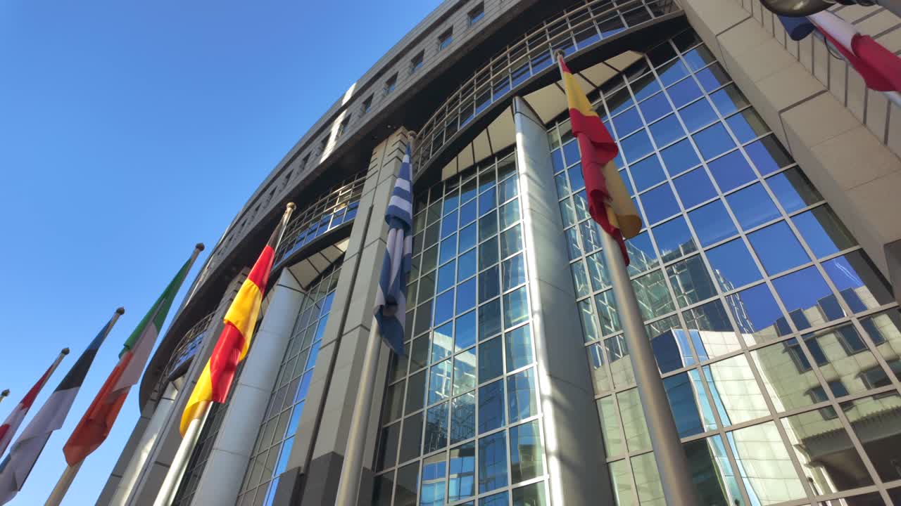Ukrainian flag waving outside modern glass facade of European Parliament