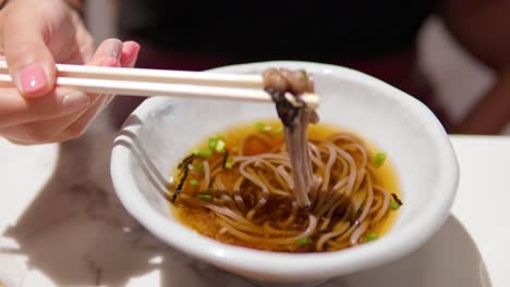 woman's hands picking up toshikoshi soba japanese buckwheat noodle with wooden chopsticks in slow motion and eat