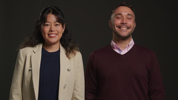 Studio Portrait Of Smiling Male And Female Teachers Walking Towards Camera And Standing Against Black Background