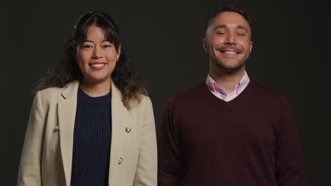 studio portrait of smiling male and female teachers walking towards camera and standing against black background