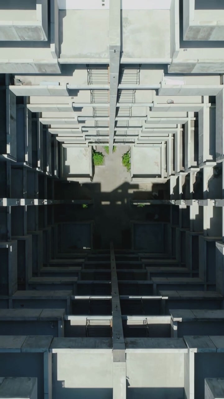 Vertical video: Descending camera revealing shaft in atrium, showing courtyard planters and shadows