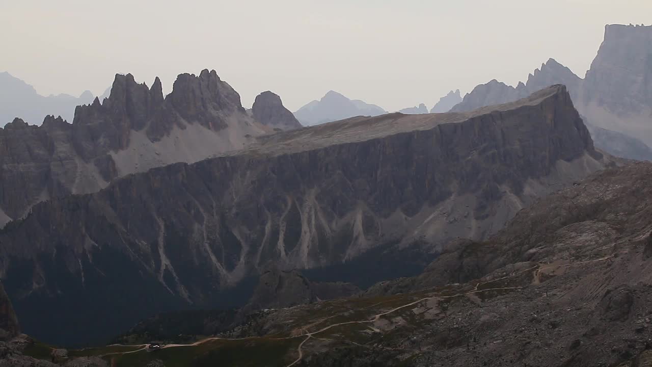 Pemandangan udara dari punggung gunung драматическая datar dengan puncak tajam di Dolomites, medan terjal di bawah cahaya siang yang lembut dengan lapisan kabut dari jajaran pegunungan Alpen yang jauh