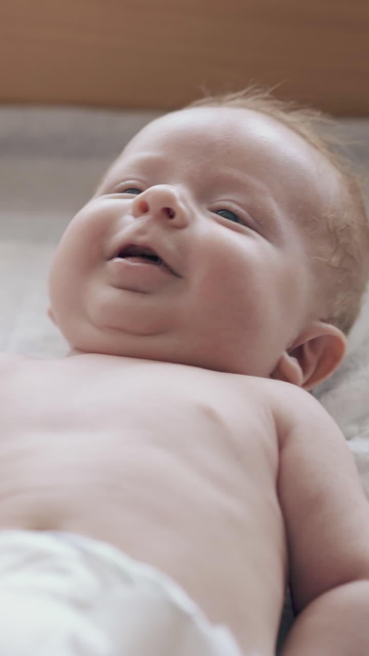 adorable fair haired infant in white diaper with hypertonus lies on changing table and enjoys legs massage close view