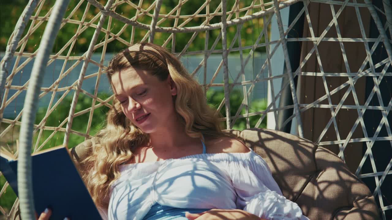 Gelukkige vrouw leest een boek in een hangstoel buiten.