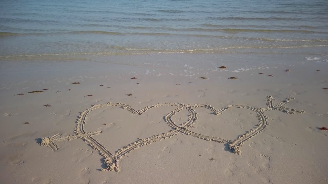 Two interlocking hearts inscribed in the sand with an arrow through them