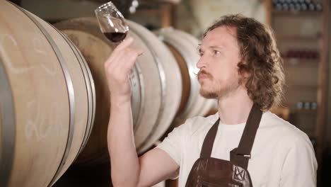 authentic shot of successful male sommelier is tasting a flavor and checking white wine quality poured in transparent glass in a wine cellar.