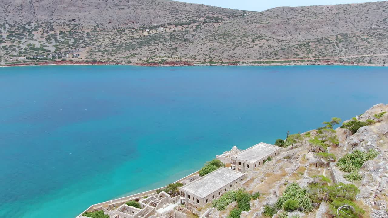 Aerial shot of Spinalonga island at Crete with clear turquoise water against a barren dry landscape. Greece