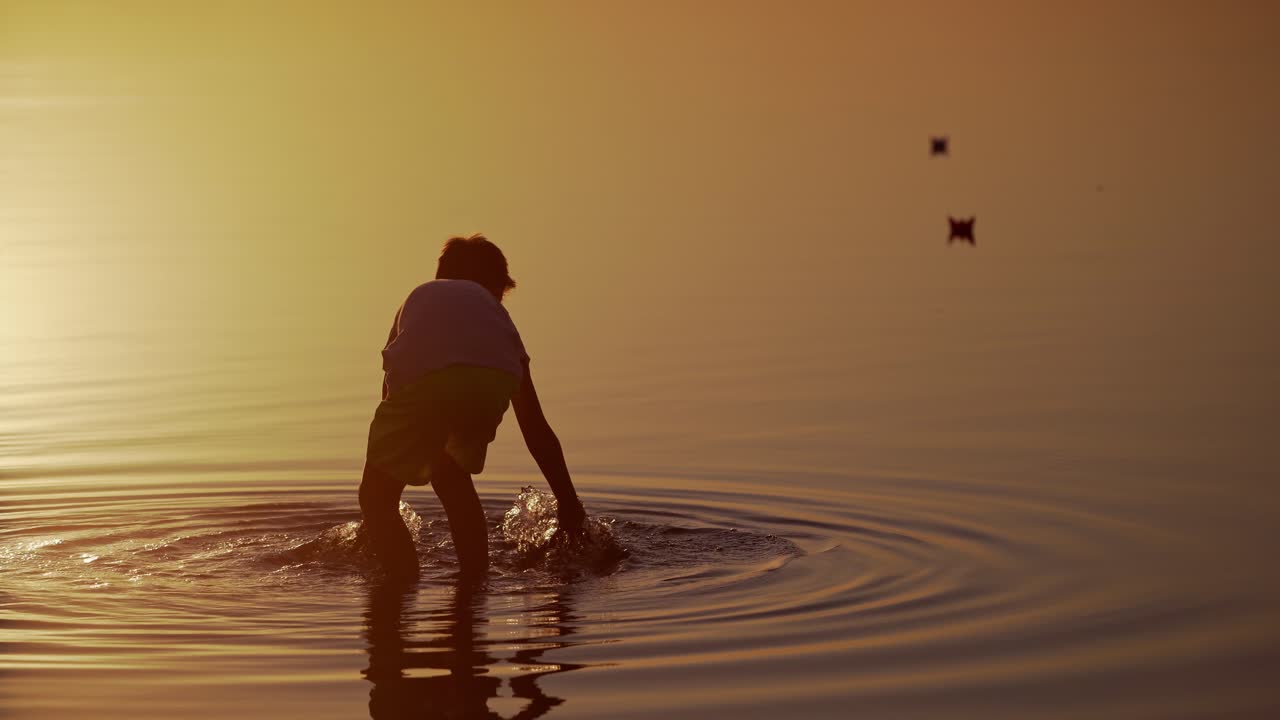 Boy launches Red and green Paper Ships in the river. Origami Paper Boats in kid's hands. Beautiful Waves Ripple Background. Travel and nature Concept. Video at sunset.