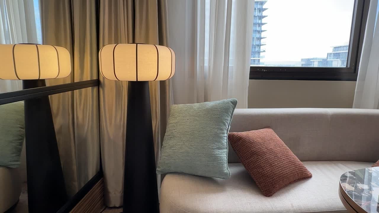 Warm cosy hotel room at Pan Pacific Perth. Stylish pedestal lamp, sofa and cushions near window.