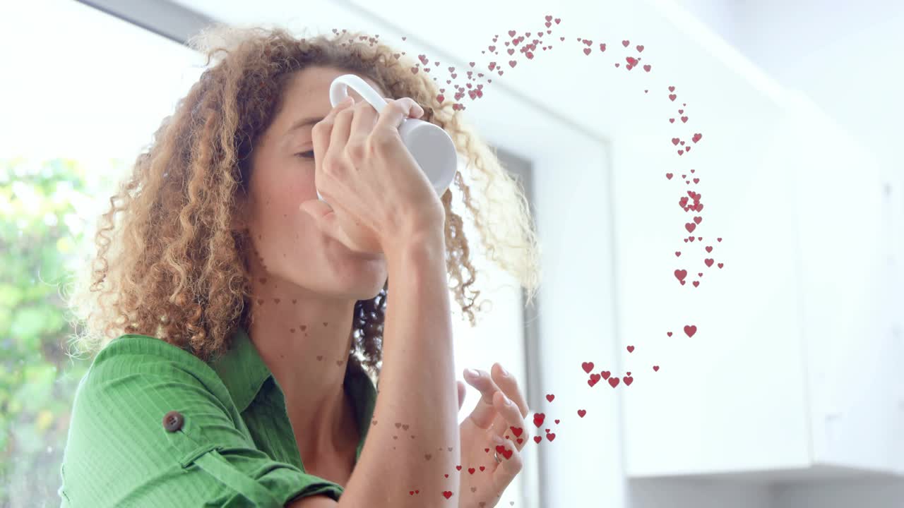 Frau greift in der heimischen Küche nach einer Tasse und nippt an einem Gesundheitstrank, wobei animierte Herzen entstehen.
