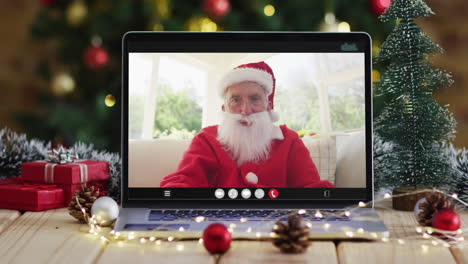 senior caucasian man in santa costume on video call on laptop, with christmas decorations and tree