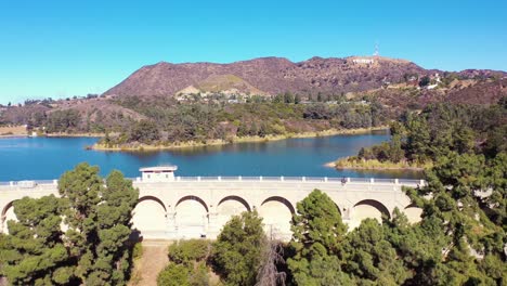 Aerial-Over-The-Dam-At-The-Hollywood-Reservoir-In-The-Hollywood-Hills-With-Hollywood-Sign-Distant