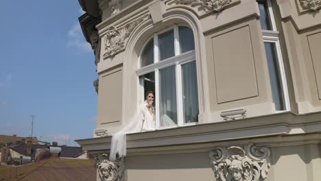 Bride-in-boudoir-dress-sitting-on-window-sill-wedding-morning-preparations-woman-in-night-gown,-veil