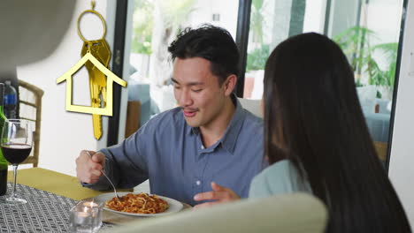 animation of gold house key and key fob over happy biracial couple eating at home