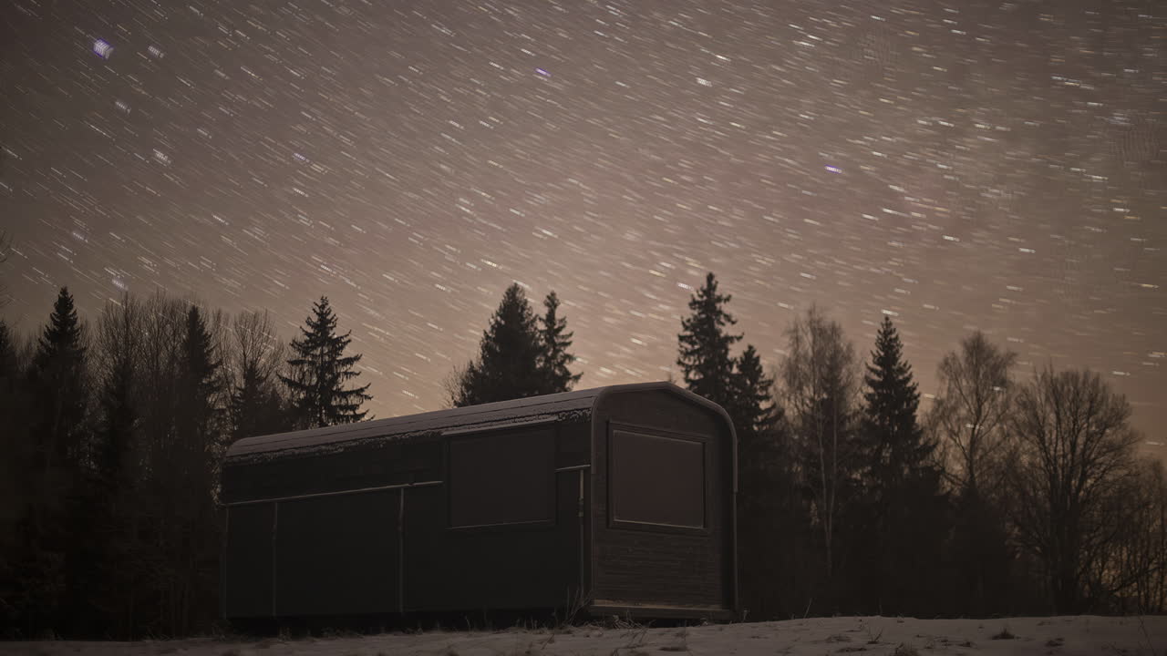 toma de tiempo del movimiento estelar sobre una pequeña cabaña rodeada de un paisaje cubierto de nieve en la noche