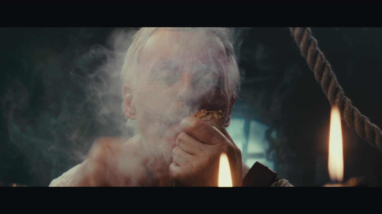 An old pirate eats and drinks and smokes a pipe inside the sailing ship cabin