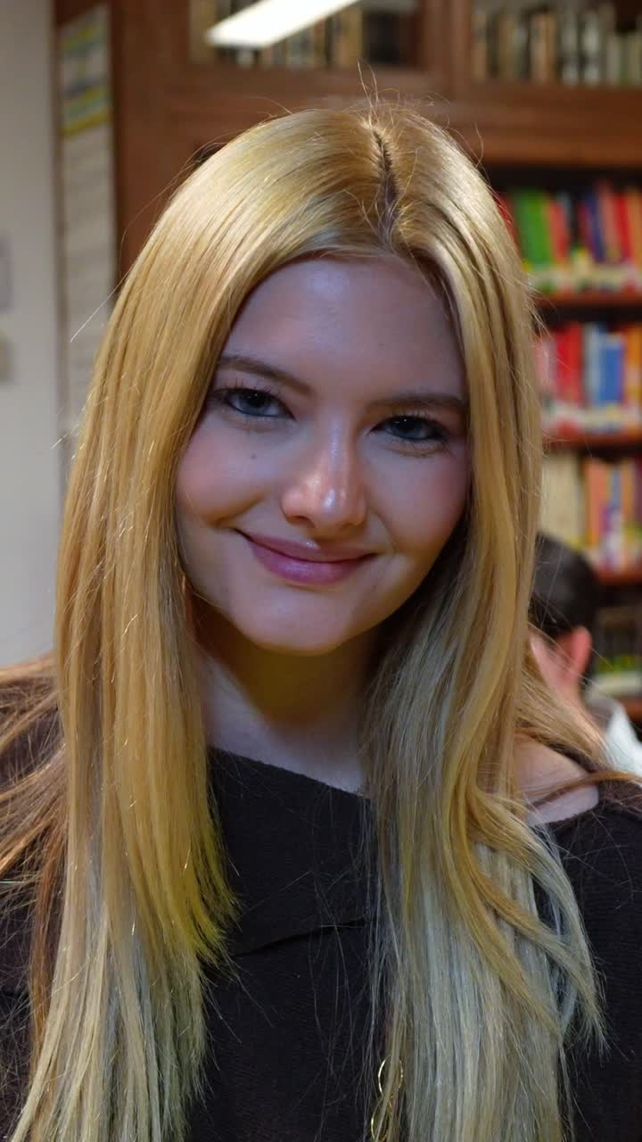 Ritratto di una studentessa bionda sorridente in una biblioteca universitaria