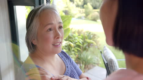 senior asian woman smiling and talking with caregiver at home, enjoying conversation