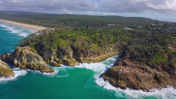 Vista aerea di una costa selvaggia con scogliere, acqua blu turchese, baia rocciosa, foresta e onde che si infrangono