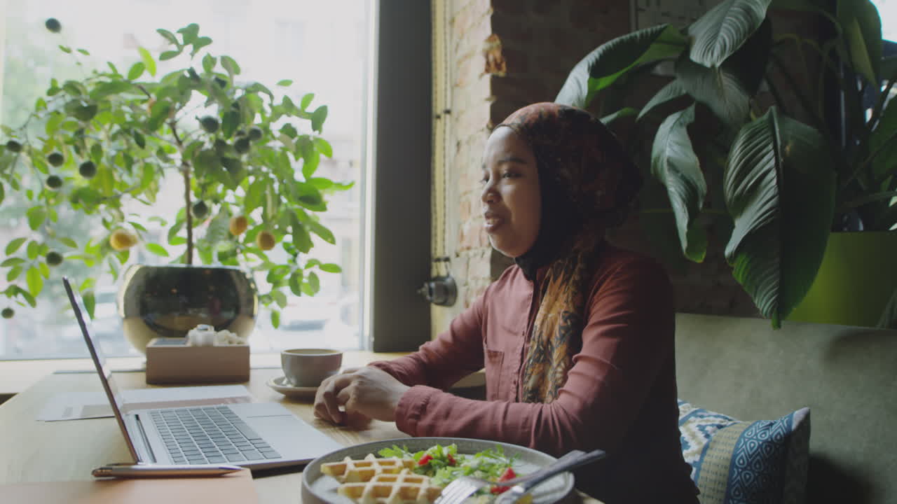 Muslim Woman Video Calling on Laptop on Lunch in Cafe