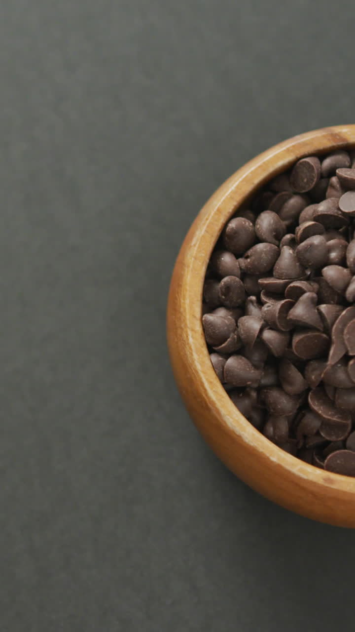Video di vista dall'alto di una ciotola di legno con gocce di cioccolato su sfondo grigio