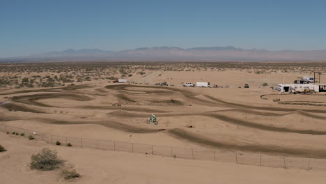 Piloto-De-Motocross-Saltando-Sobre-Una-Pista-De-Tierra-Escarpada-En-Cámara-Lenta,-Bandeja-De-Seguimiento-Aéreo